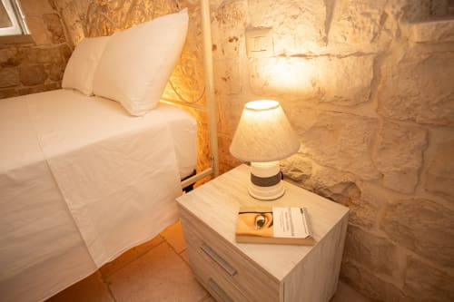 Camera accogliente nell'hotel Trulli Life, Ostuni, con biancheria bianca, muri in pietra e lampada da comodino