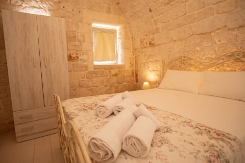 Accogliente camera in pietra al Trulli Life di Ostuni con asciugamani arrotolati sul letto, armadio in legno e illuminazione calda