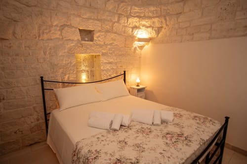Camera in pietra accogliente all'hotel Trulli Life di Ostuni con biancheria bianca, letto in ferro e illuminazione calda