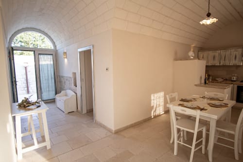 Zona pranzo Trulli Life Ostuni con tavolo bianco, sedie, cucina a vista, arco con accesso esterno nella camera Terra Rossa