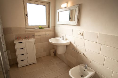 Spazioso bagno dell'hotel Trulli Life a Ostuni con doppio lavabo, lavandino a colonna, finestra e piastrelle beige