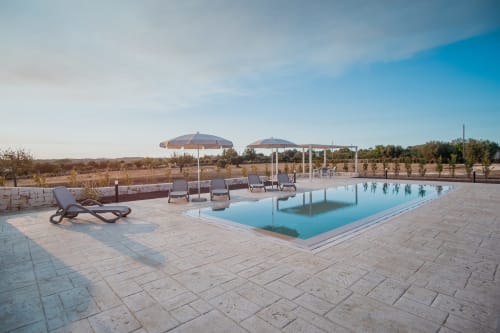Area piscina lussuosa dell'hotel Trulli Life a Ostuni con lettini, ombrelloni e vista sul paesaggio arido