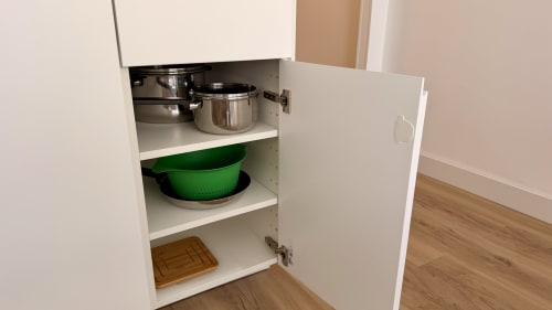 Armario de cocina abierto en Holidays Costa Brava con ollas, colador y tabla de madera en los estantes