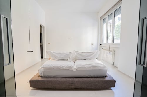 Camera da letto minimalista all'Appartamento Zen Seaside di Genova con biancheria bianca su letto grigio rialzato, grandi finestre luminose e spazi puliti