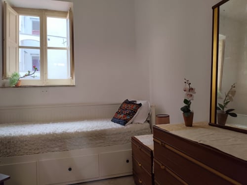 Camera accogliente al Mappamondi B&B di Venezia con letto bianco, comò in legno, specchio, piante in vaso e finestra con vista sul