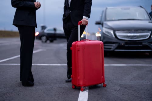 Viaggiatore d'affari con valigia rossa all'aeroporto di Palermo vicino a veicoli di lusso e SUV