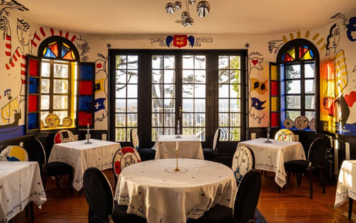 Elegant dining room at Clos Céleste with colorful Mondrian-style windows, white tablecloth tables, and artistic wall murals