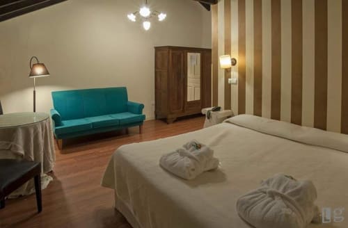 Spacious double room at Posada Torre del Milano in Comillas with bed, turquoise sofa, striped walls and wooden furnishings
