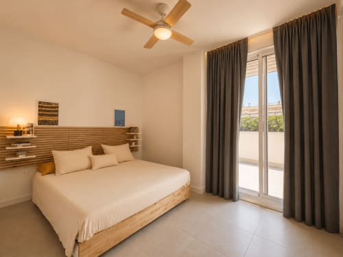 Bright bedroom at Living Sur, Sanlúcar de Barrameda, with wooden bed, ceiling fan, and terrace doors overlooking city