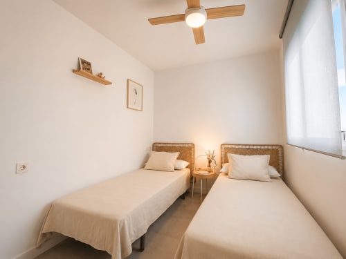Twin bedroom with wicker headboards, ceiling fan, and city view at Living Sur apartments in Sanlúcar de Barrameda