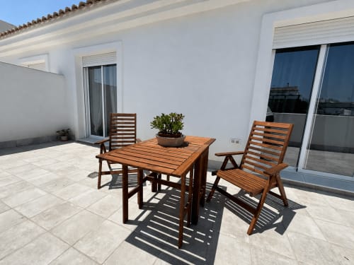Wooden outdoor dining set on sunny terrace at Living Sur apartment, Sanlúcar de Barrameda with city views