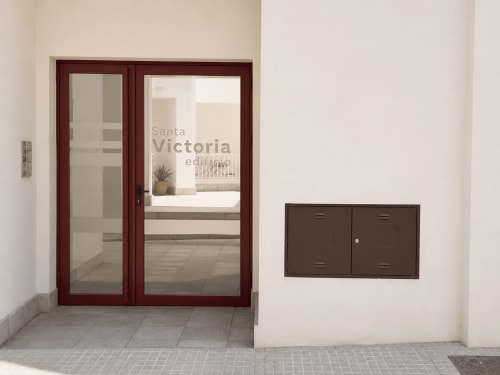 Modern apartment entrance at Living Sur hotel in Sanlúcar de Barrameda with dark red framed glass doors and mailboxes on