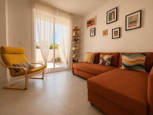 Modern apartment living room with rust-orange sofa, yellow accent chair, and city views at Living Sur, Sanlúcar de Barrameda