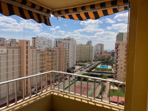 Vista desde el balcón del ML Apartments en Picanya con toldo rayado, dominando edificios residenciales y piscina común