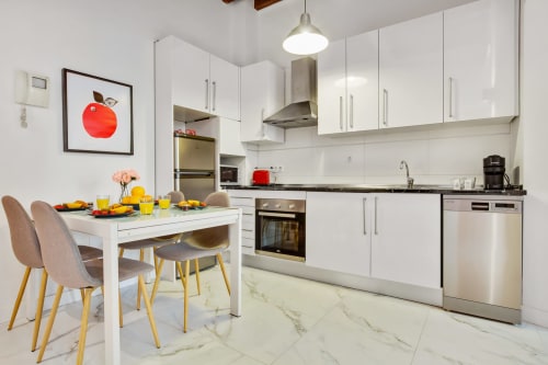 Modern white kitchen and dining area in Ayma Apartamento Ollerías, Málaga with marble flooring and stainless steel appliances