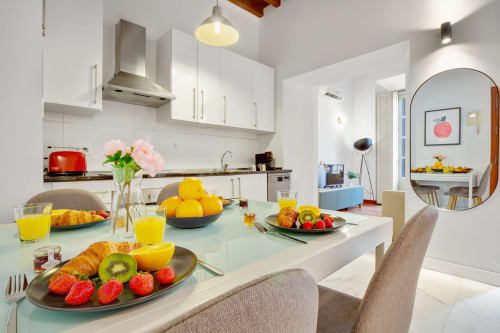 Modern Málaga apartment kitchen and dining area with fresh fruit, breakfast spread, and contemporary white cabinetry