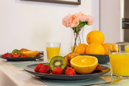 Breakfast table with fresh fruits, orange juice, and pink carnations at Ayma Apartamento Ollerías, Málaga