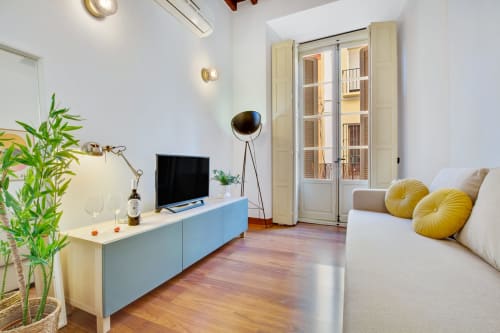 Modern living room in Ayma Apartamento Ollerías, Málaga with blue TV unit, cream sofa, yellow pillows, bookshelf, and wooden