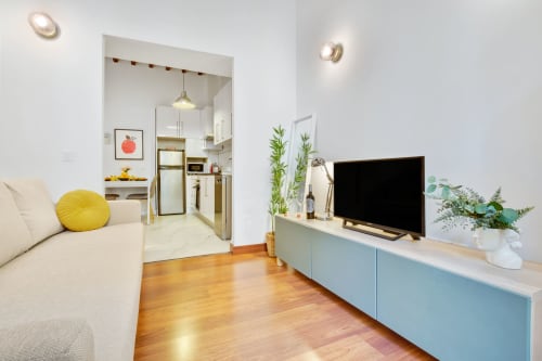 Modern Málaga apartment living room with TV, kitchen view, wooden floors, and indoor plants