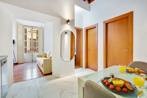 Modern Málaga apartment kitchen and dining area with marble floors, wooden doors, and fresh fruit breakfast setup