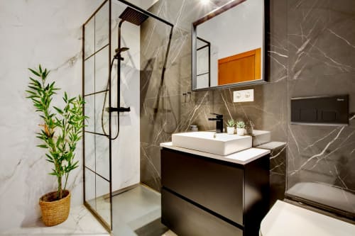 Modern bathroom in Ayma Apartamento Ollerías, Málaga with marble walls, black vanity, white sink, rain shower, and potted