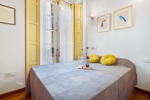 Bright bedroom at Ayma Apartamento Ollerías in Málaga with yellow doors, blue bedding, and bird artwork on white walls.