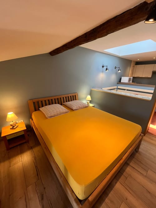 Chambre loft moderne au Jardin De Palme avec literie orange, poutres bois, lucarne et vue sur le jardin
