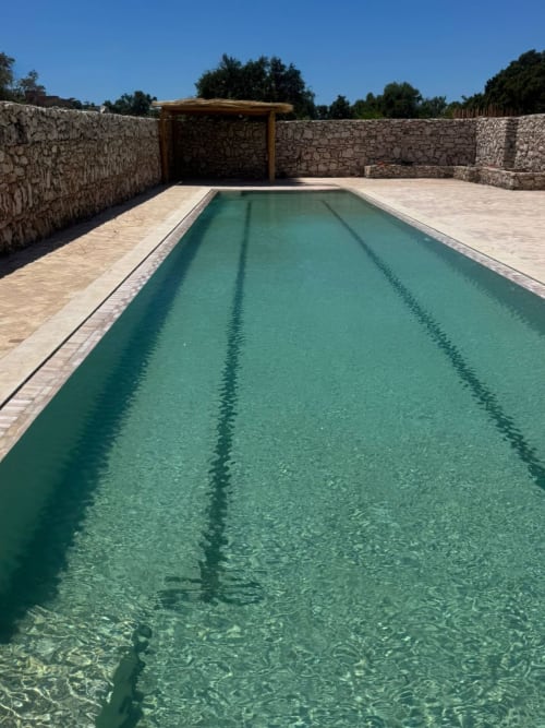 Piscine rectangulaire aux eaux turquoise du Domaine Belhazar à Essaouira, encadrée de murs en pierre et d'une pergola en bois