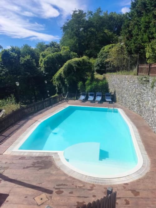 Piscina a forma di L con acqua turchese, lettini prendisole e rigogliosi alberi verdi presso Welcome Holiday apartment a Calice