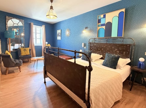 Dormitorio elegante en azul en el Hôtel La Suite de Villeneuve-lès-Avignon con cama de hierro, arte moderno y pisos de madera.