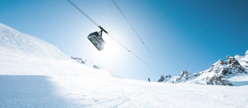 Téléphérique montant la piste enneigée de la station de ski de Courchevel avec un terrain blanc immaculé en contrebas