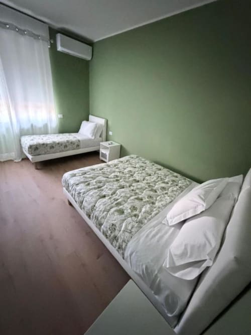Camera tripla presso 88 Destination a Treviglio con due letti, pareti verdi, cuscini bianchi e climatizzatore