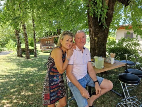 Deux clients savourent leurs boissons à une table sous les arbres dans le jardin ensoleillé de Zoppas Courchevel, un hôtel de montagne français