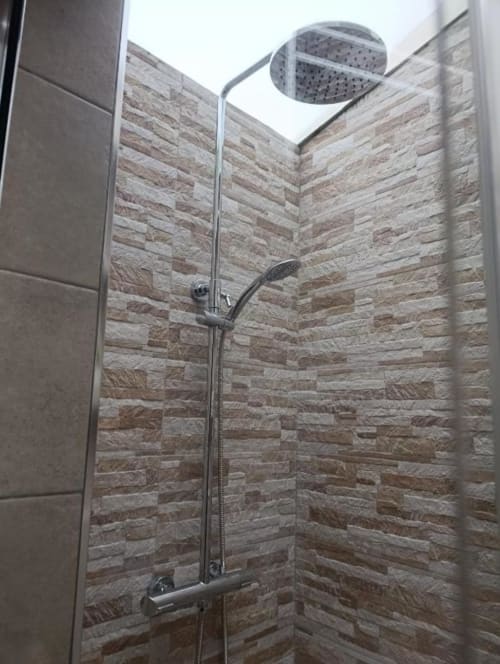 Moderno cuarto de baño con ducha, paredes de azulejos de piedra y alcachofa de lluvia en la villa Sol de Antequera