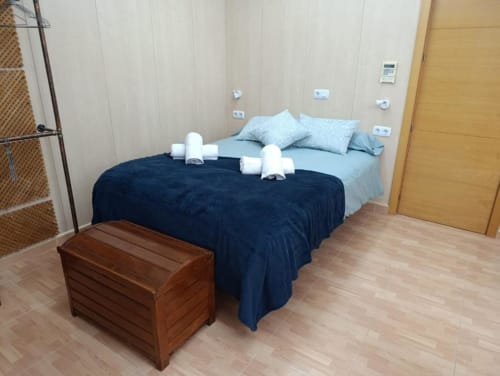 Dormitorio moderno en villa Sol de Alojamientos Las Mellis, Antequera, con ropa de cama azul, almohadas claras, banco de madera y luz natural