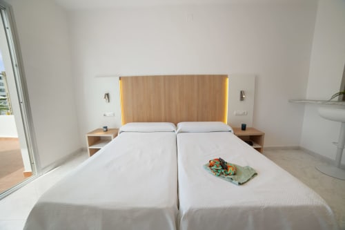 Dormitorio de estudio moderno en Apartamentos Playa Sol con camas gemelas, cabecero de madera, vistas a la montaña y balcón