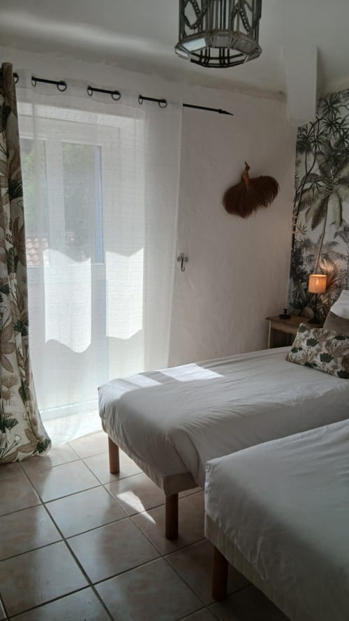 Chambre lumineuse à La Ribeyrette avec lits jumeaux, papier peint tropical, portes vitrées et suspension décorative