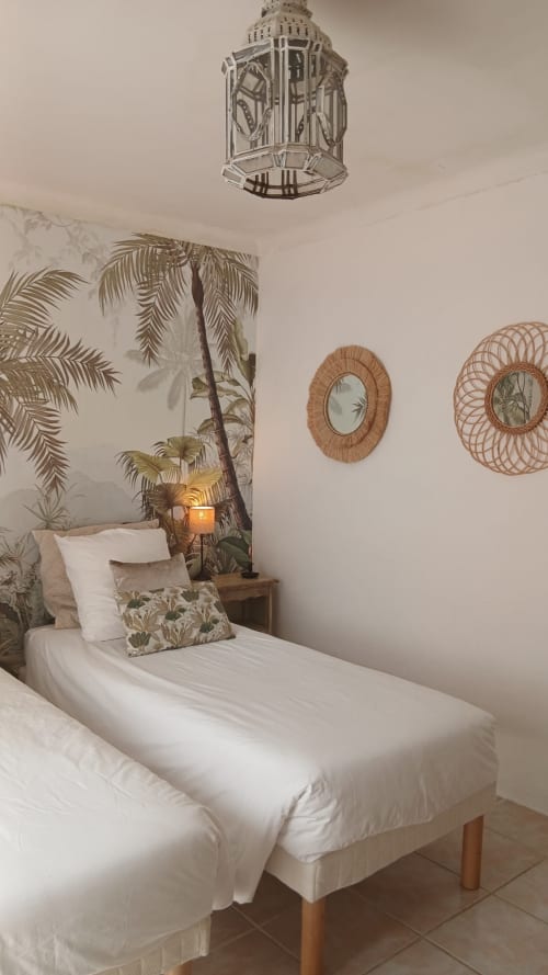Chambre cosy du gîte La Ribeyrette à Chamborigaud avec lit simple, papier peint tropical, miroirs tressés et suspension décora
