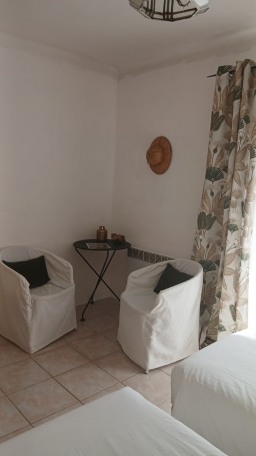 Espace détente de La Ribeyrette B&B avec fauteuils blancs, rideaux botaniques et décoration murale en bois à Chamborigaud