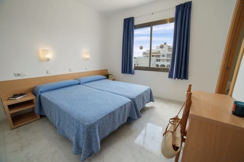 Dormitorio luminoso de apartamento estándar en Apartamentos Playa Sol en Es Canar con camas gemelas, ropa de cama azul y vistas a la ciudad