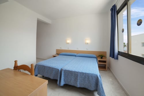Luminoso dormitorio de apartamento estándar en Apartamentos Playa Sol en Es Canar con cama azul y vistas a la montaña desde gran ventana