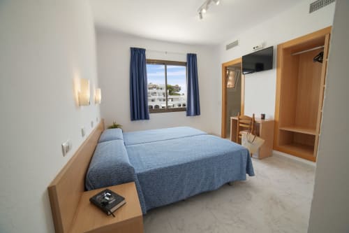 Dormitorio estándar en Apartamentos Playa Sol, Es Canar, con ropa de cama azul, muebles de madera y vistas a la montaña
