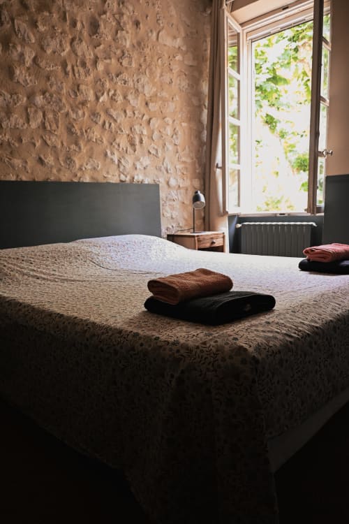 Chambre rustique au Mas De La Digue B&B à Châteaurenard avec serviettes pliées sur le lit, mur en pierre texturée et fenêtre ouverte