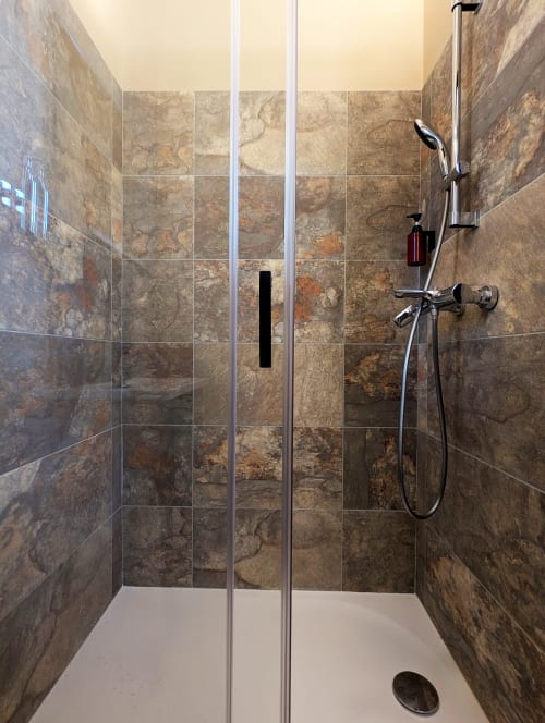Salle de bain moderne du gîte Domaine Alga avec douche italienne, carrelage en travertin, pommeau de douche cascade et douchette à main