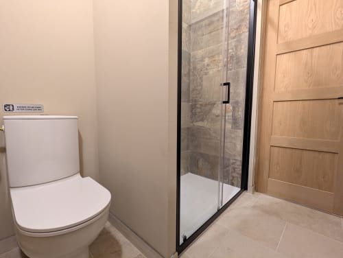 Salle de bain moderne du gîte Domaine Alga avec douche vitrée, toilettes et porte en bois à Bourg-Charente
