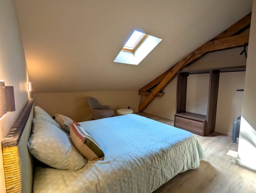 Chambre spacieuse sous les toits au gîte Domaine Alga avec lucarne, poutres bois, literie bleue et lumière naturelle