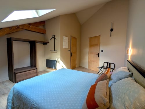 Chambre spacieuse du gîte Domaine Alga à Bourg-Charente avec literie bleue, poutres en bois, lucarne et équipements modernes