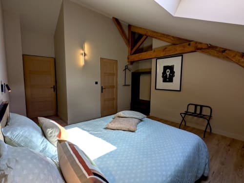 Chambre spacieuse au gîte Domaine Alga à Bourg-Charente avec poutres apparentes, literie bleue, portes en bois et équipements modernes