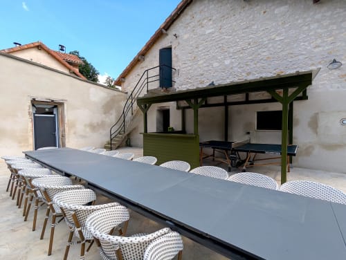 Zone de repas extérieure du gîte Domaine Alga à Bourg-Charente avec longue table, chaises en osier et espace de détente couvert