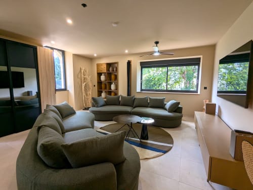 Salon moderne du gîte Domaine Alga à Bourg-Charente avec canapé gris incurvé et grandes fenêtres sur la verdure